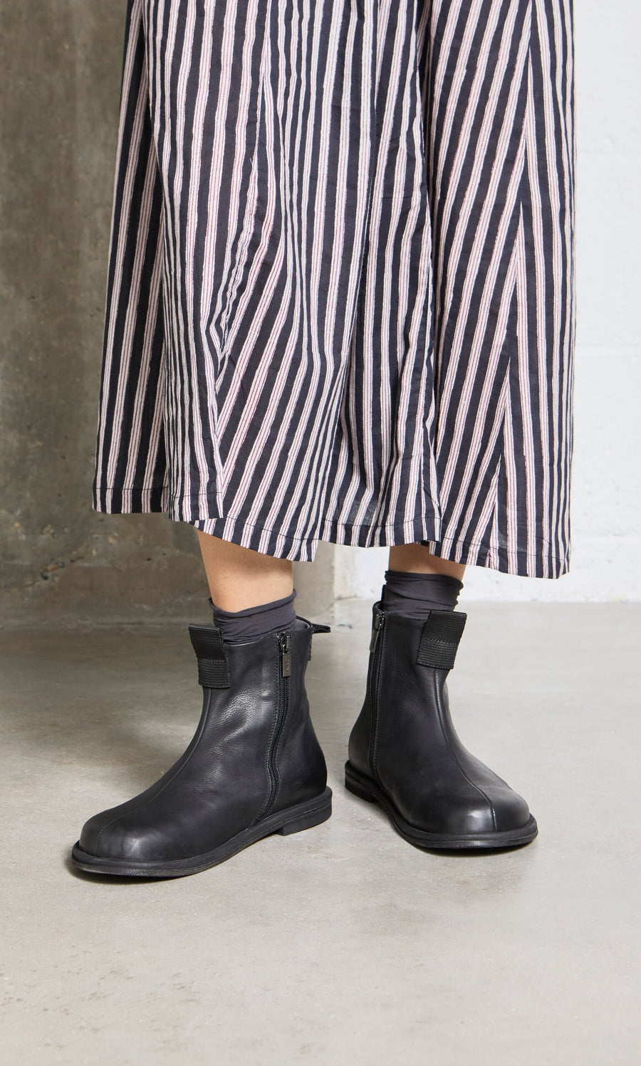 Plümo- Person wearing a long, striped skirt and Ancona Boots, standing on a concrete floor.
