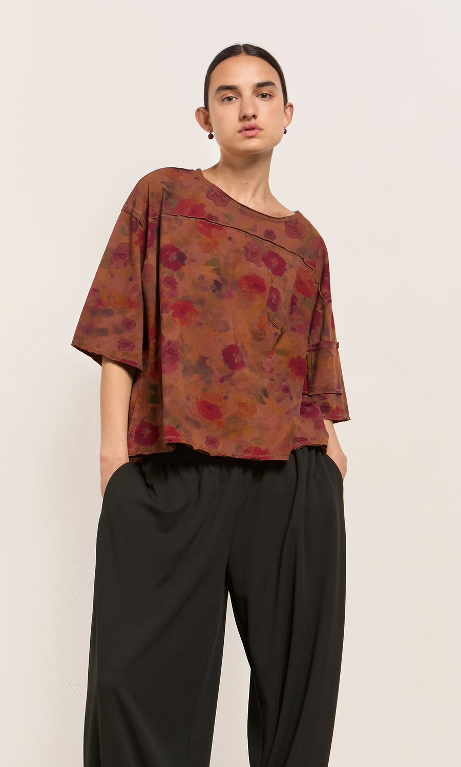 Plümo  Model in Angie Tee with an impressionistic floral print and black wide-leg pants against a plain light background.