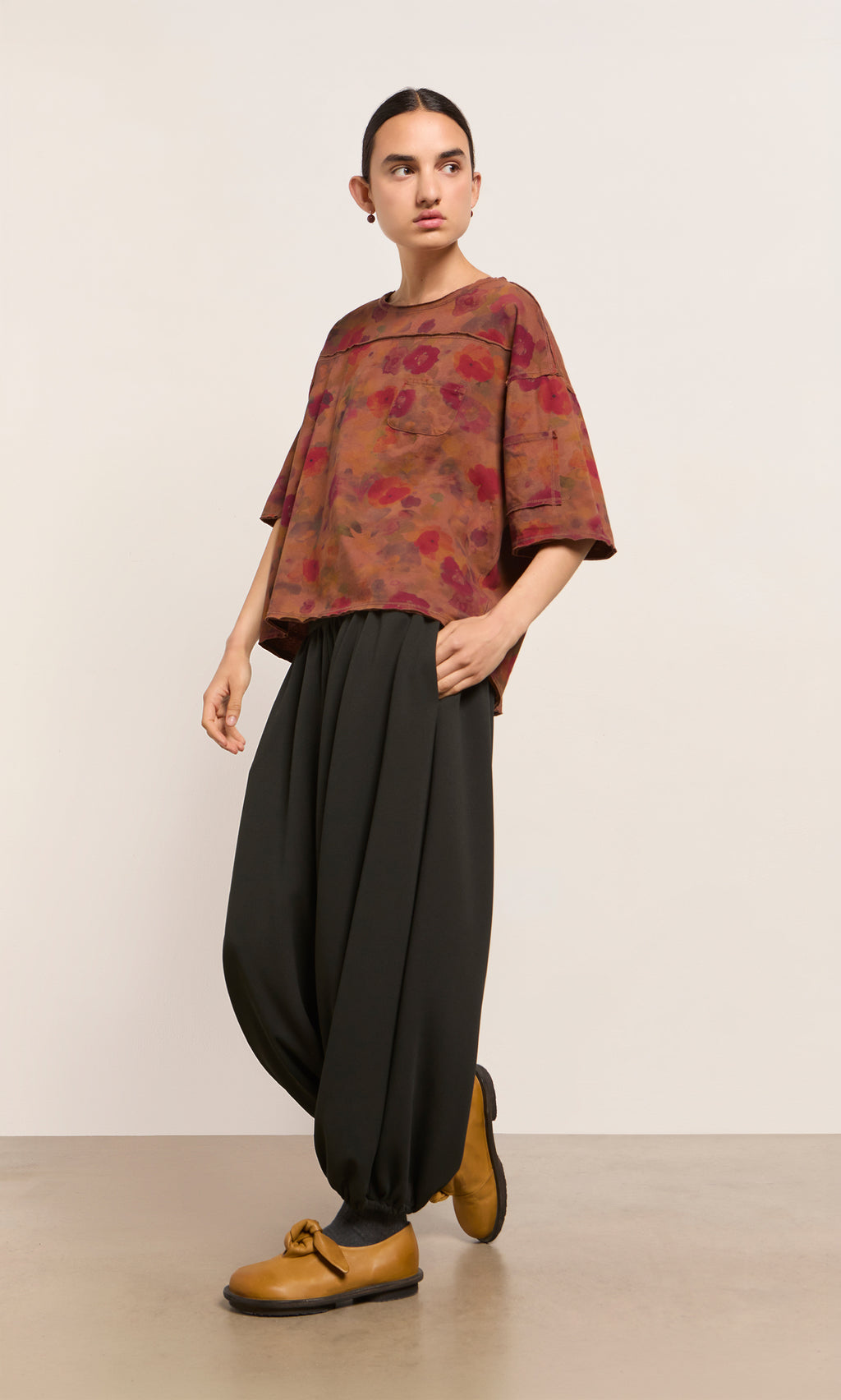 Plümo  Person in a floral red top, Mia Balloon Pants, and yellow shoes stands against a plain background, looking to the side.
