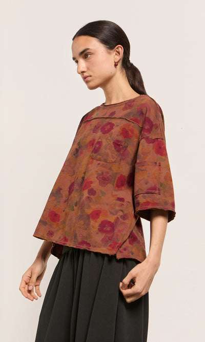 Plümo  Woman in a loose Angie Tee with red floral print and elbow sleeves, paired with a black skirt against a plain background.