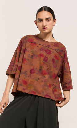 Plümo  Model wears the Angie Tee in an impressionistic floral print with black pants, posed against a plain background.