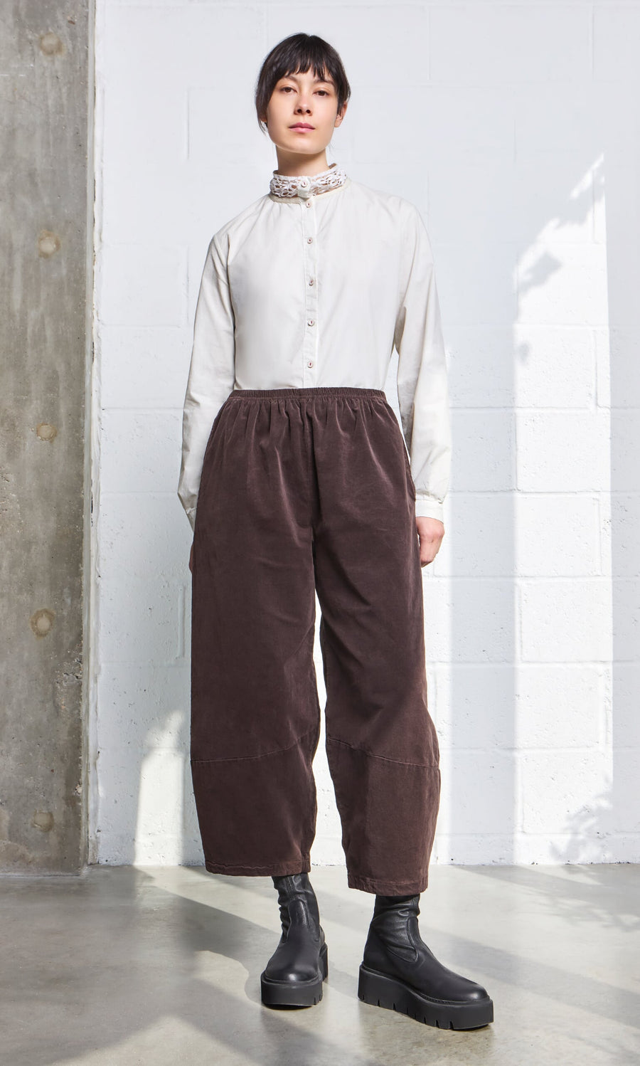 Plümo - A woman in a white blouse and Anise Pants with an elasticated waistband stands in natural light.