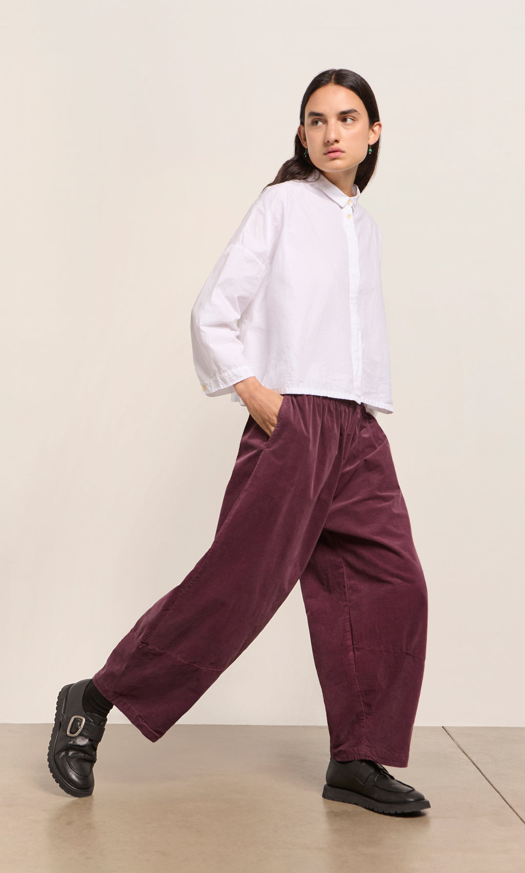 Plümo  Person in white button-up and Architect Pants - Lupins walks forward, hands in pockets, on a plain background.