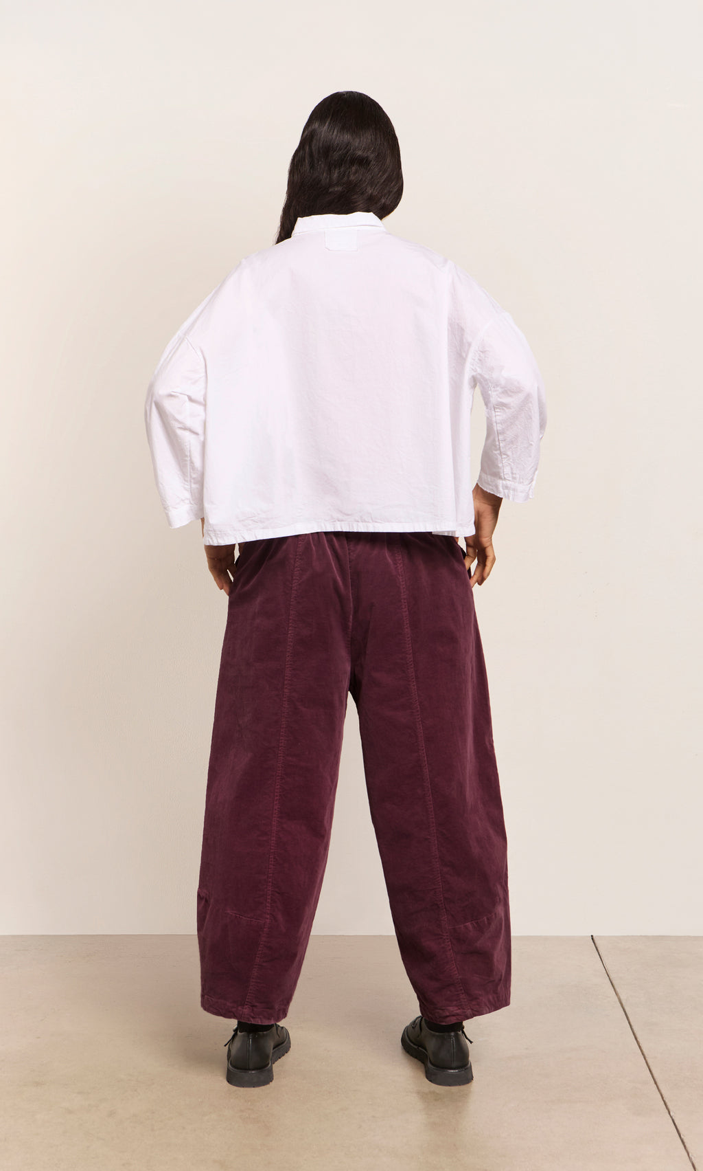 Plümo  Person stands with back to camera in a white shirt and Architect Pants - Lupins on a plain background.