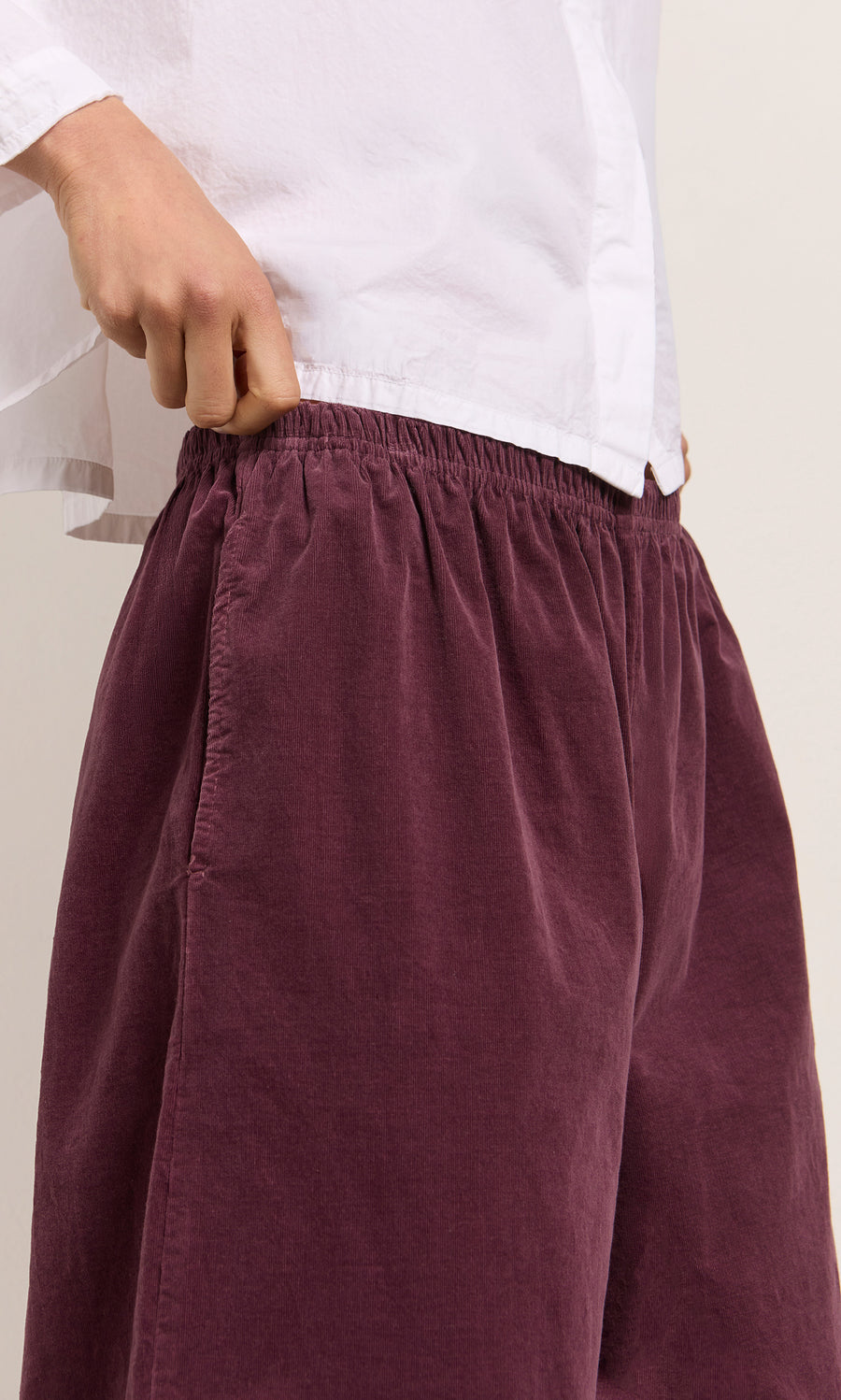 Plümo  Someone in a white shirt holds the waistband of maroon Architect Pants - Lupins with an elastic waist.