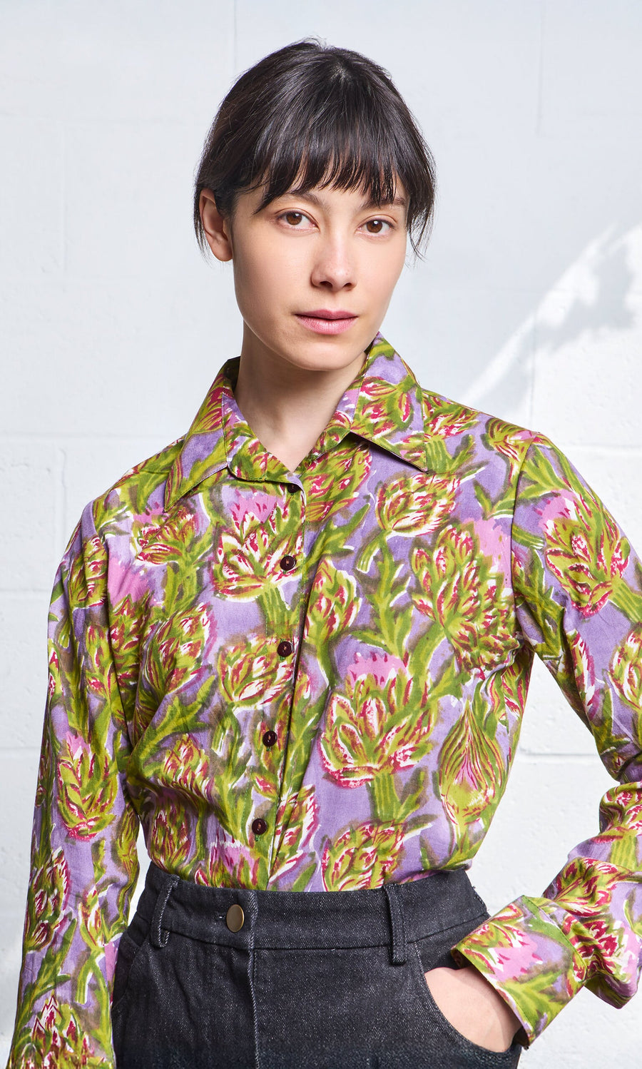 Plümo- Woman wearing the Artichoke Shirt, a colorful block-printed cotton top, with high-waisted dark pants.