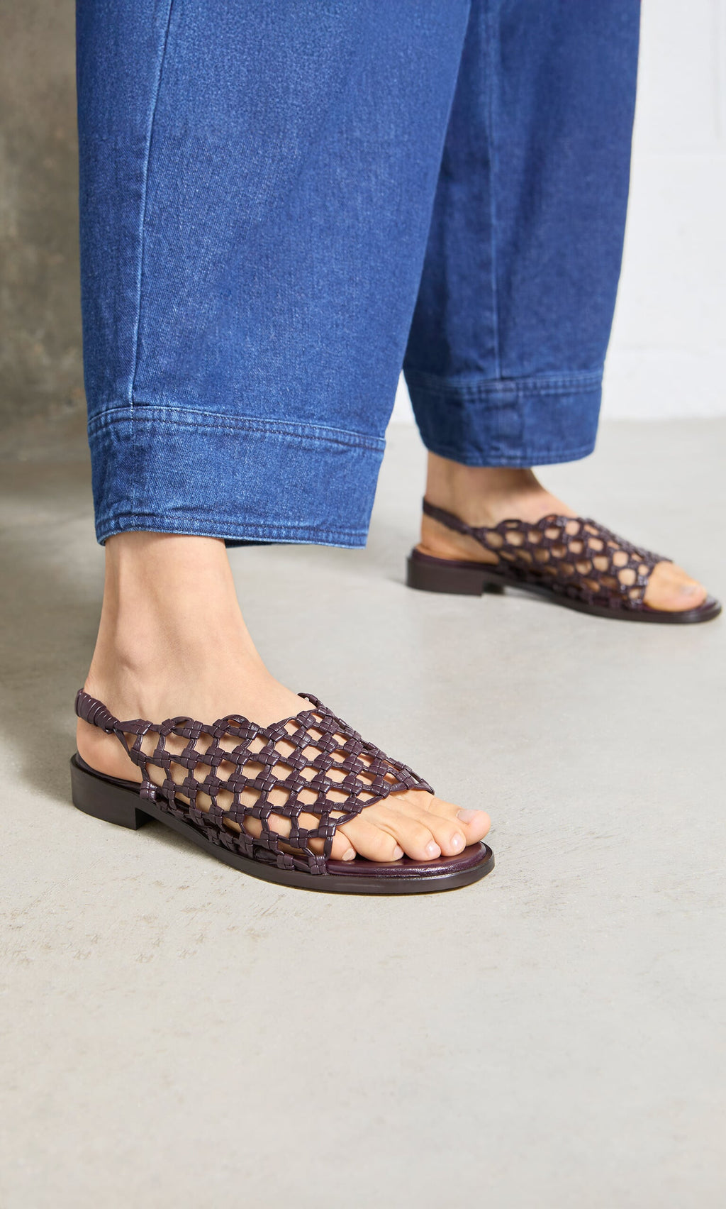 Plümo- Person wearing wide-leg blue jeans and Arts Club Sandals, handcrafted brown peeptoe leather, on a light floor.
