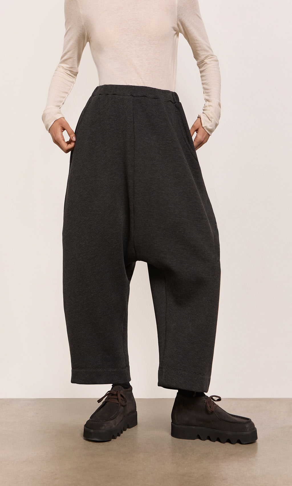 Plümo  Person in Asker Grey Pants, beige long-sleeve shirt, and black shoes stands on a plain floor.