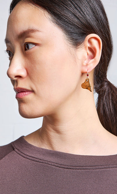 Plümo- Woman with dark hair in a ponytail, wearing a brown shirt and Bacio Earrings, looks to the left.