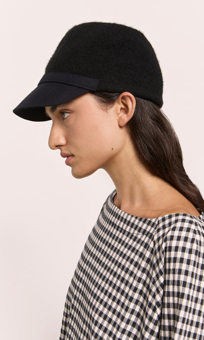 Plümo  Woman in a Baseball Cap and checkered top, shown in profile against a plain light background.