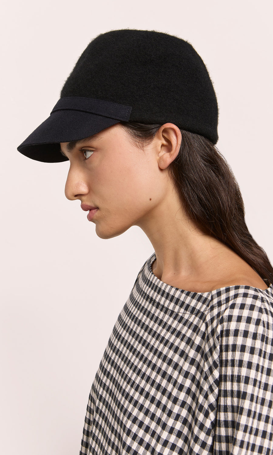 Plümo  Woman in a Baseball Cap and checkered top, shown in profile against a plain light background.