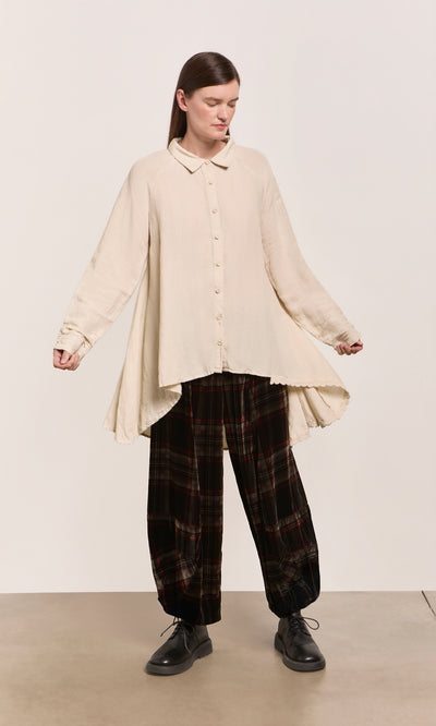 Plümo  Someone in the Beeson Shirt - Oat and plaid pants stands on a light floor against a plain backdrop.