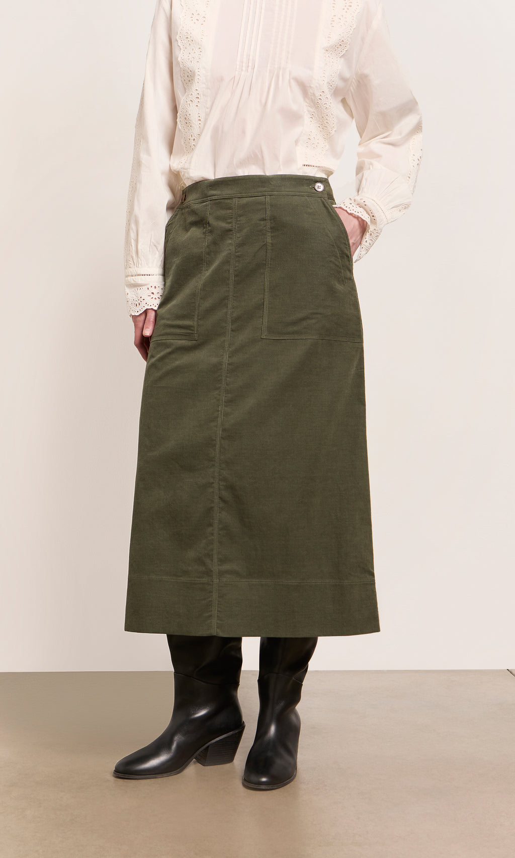 Plümo  Person wearing a white blouse, Beetle Green Skirt, and black boots against a plain background.