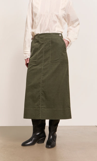 Plümo  Person wearing a white blouse, Beetle Green Skirt, and black boots against a plain background.