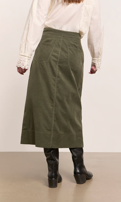 Plümo  Woman in cream blouse and Beetle Green Skirt, FSC certified cotton needlecord, black boots, back to camera.