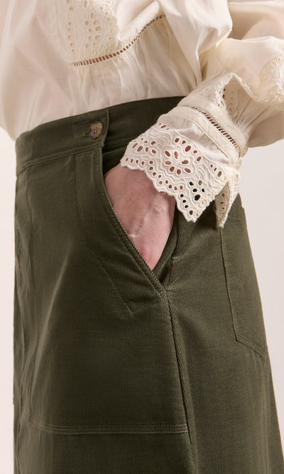 Plümo  A person wears an ivory lace blouse and the Beetle Green Skirt, one hand tucked casually in the skirt pocket.