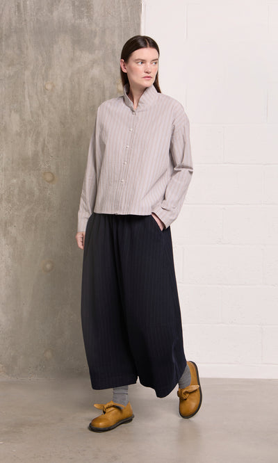 Plümo  Person in the Bennett Blouse - Smoke stands against a concrete and white brick wall.