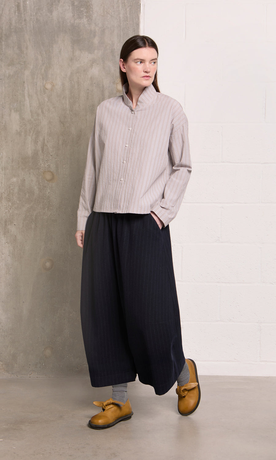 Plümo  Person in the Bennett Blouse - Smoke stands against a concrete and white brick wall.
