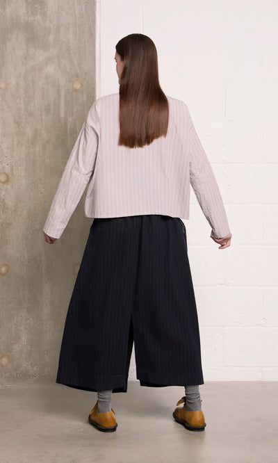 Plümo  A person faces away in wide dark pants and the Bennett Blouse - Smoke, yellow shoes, long brown hair.