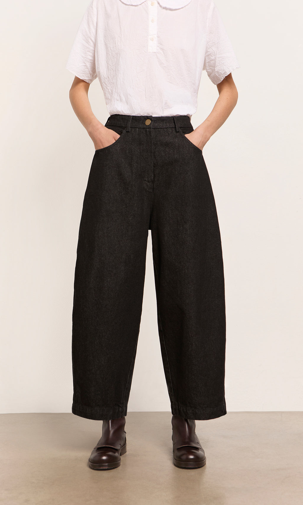 Plümo  Person in a white shirt, Black Barrel Pants with a relaxed silhouette, and dark boots, hands in pockets.