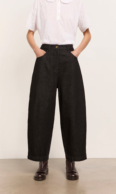 Plümo  Person in a white shirt, Black Barrel Pants with a relaxed silhouette, and dark boots, hands in pockets.
