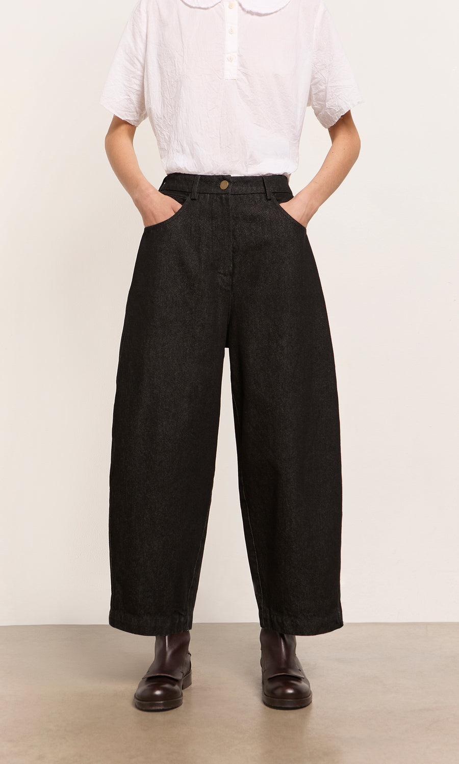 Plümo  Person in a white shirt, Black Barrel Pants with a relaxed silhouette, and dark boots, hands in pockets.