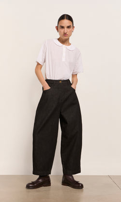 Plümo  Person in a white shirt and Black Barrel Pants stands against a plain background.