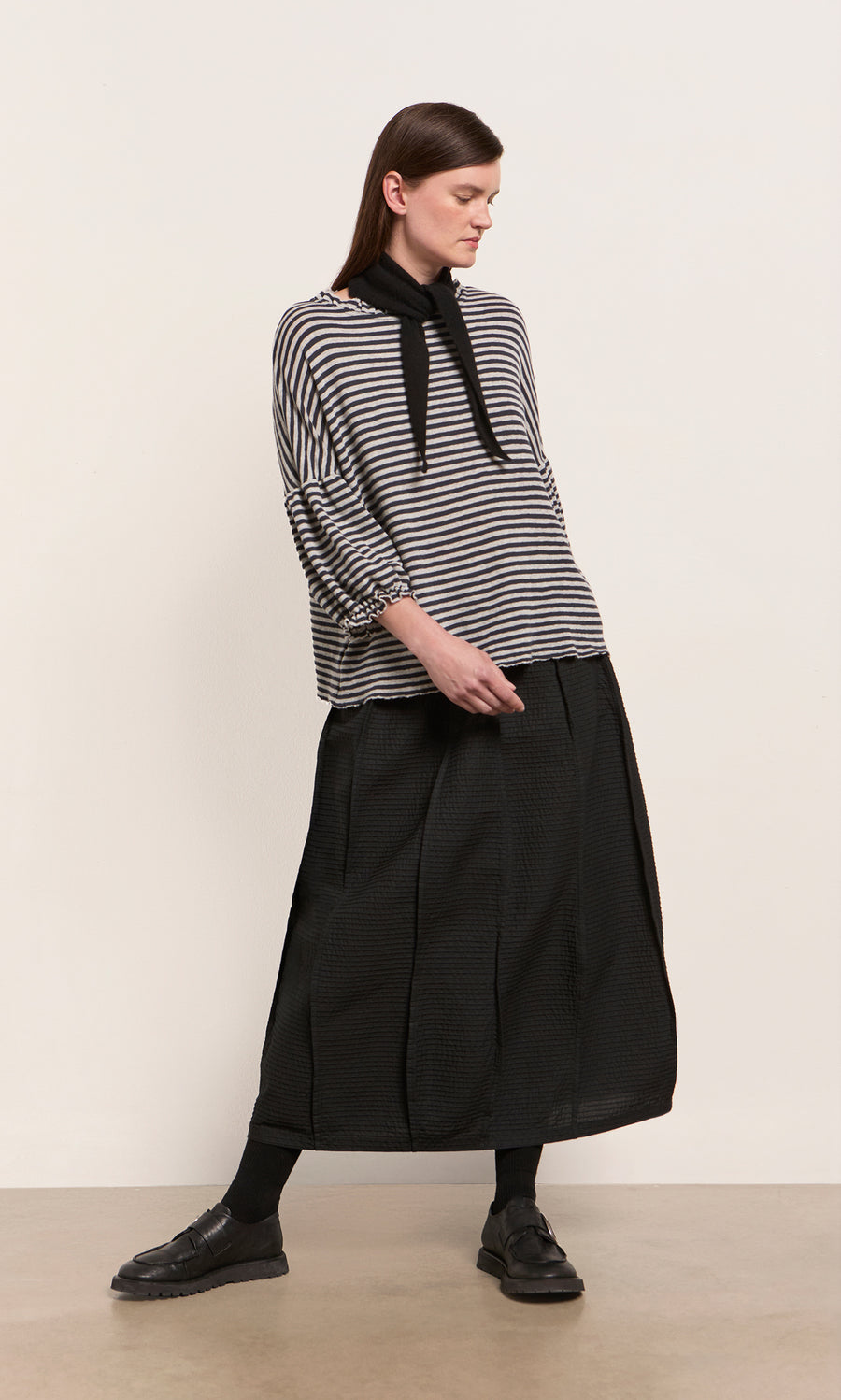 Plümo  Woman in a striped top and black skirt styles her look with a Black Cashmere Necktie for a touch of Danish flair.