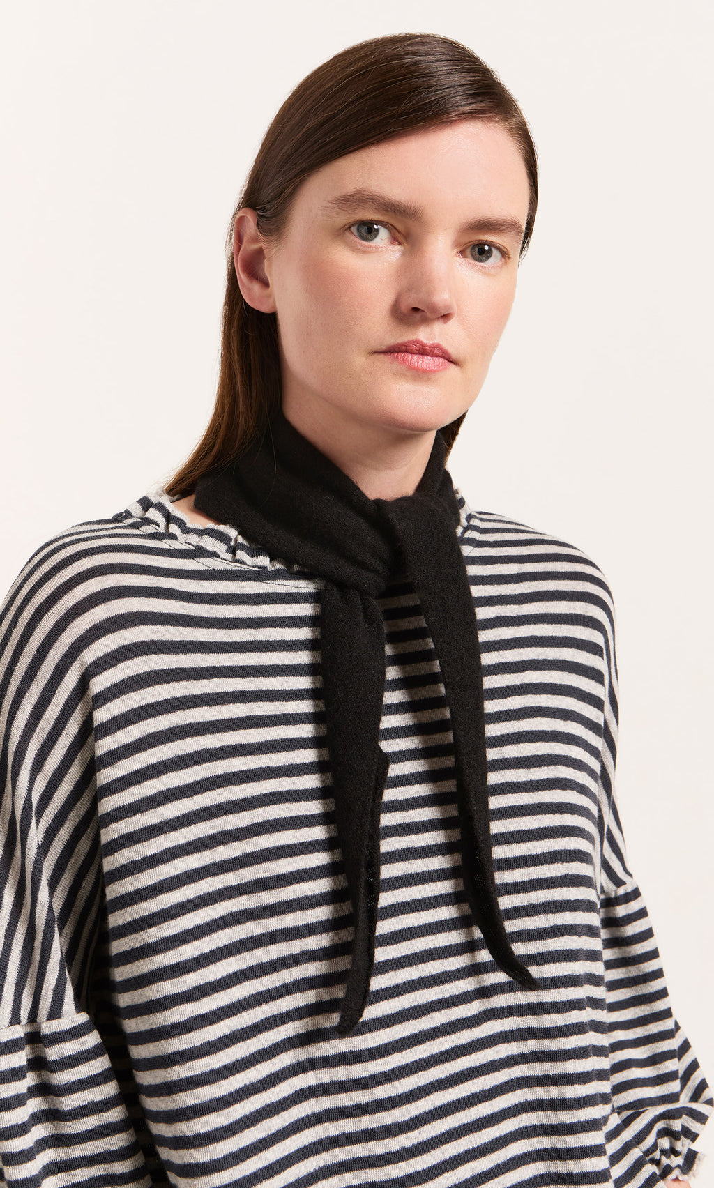 Plümo  Woman in striped shirt wearing a Black Cashmere Necktie, looking at the camera—a chic accessory for winter.