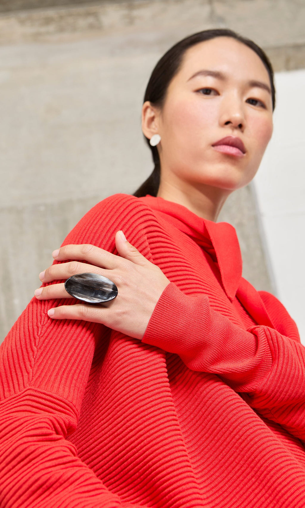 Plümo- Woman in a red sweater wearing a Black Oval Ring, showcasing handmade jewelry and looking confidently at the camera.