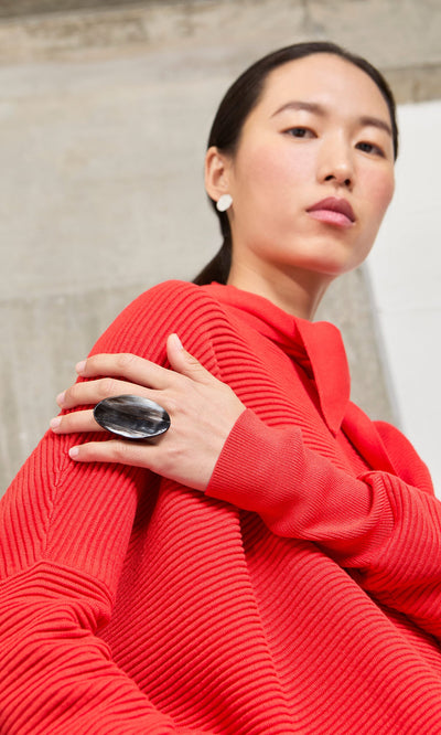 Plümo- Woman in a red sweater wearing a Black Oval Ring, showcasing handmade jewelry and looking confidently at the camera.
