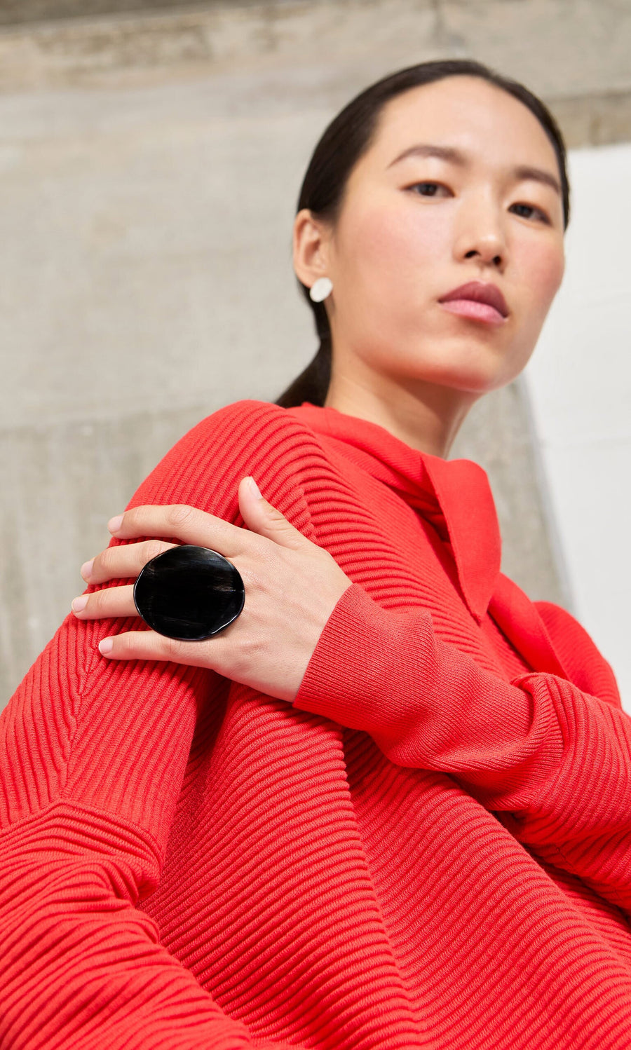 Plümo- Woman in a red textured outfit showcases the Black Circle Ring, a handmade modern design, looking confidently at the camera.