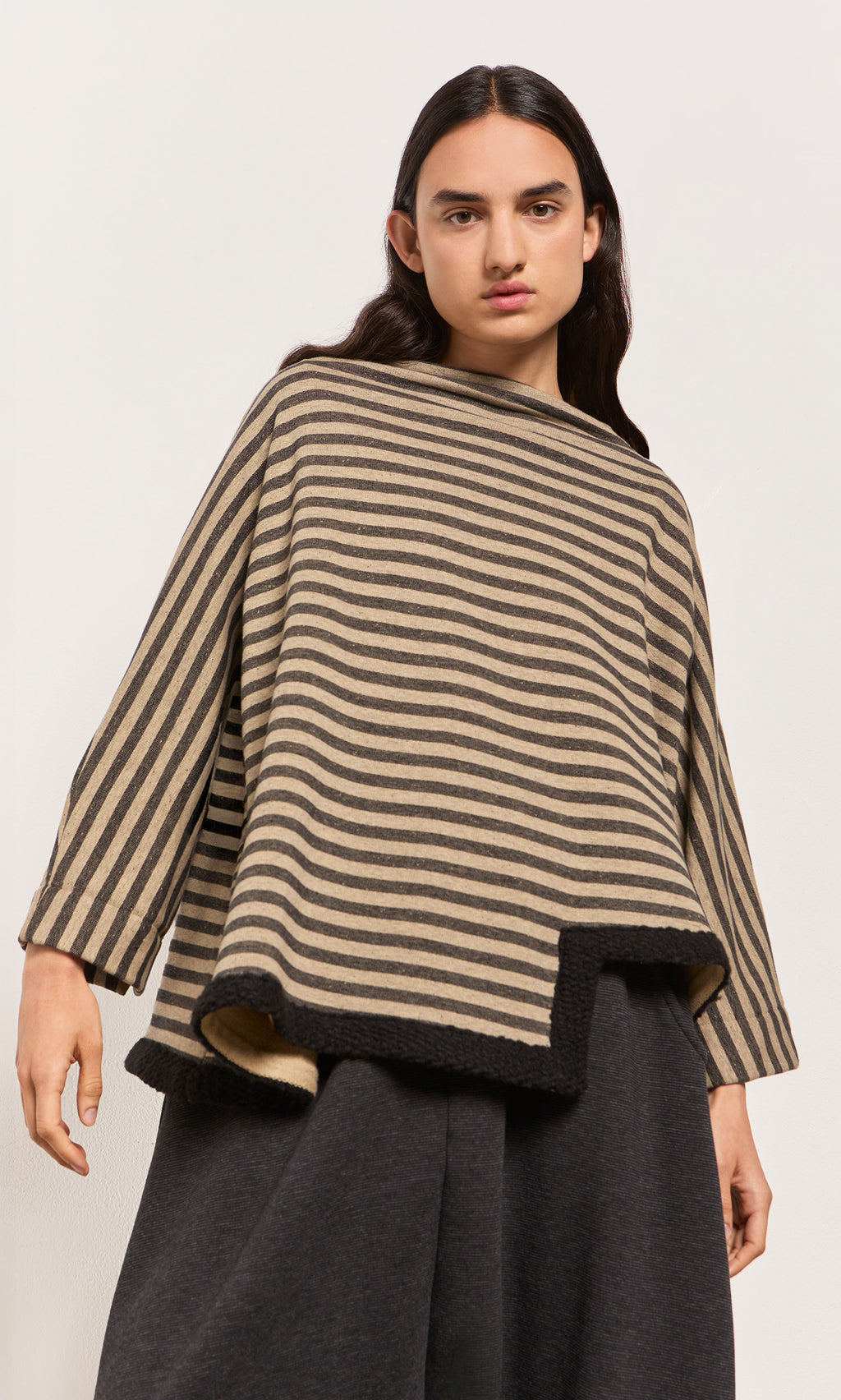 Plümo  A model wears the Bloch Funnel Top in taupe and black stripes with wide sleeves and an asymmetric cut-out hem.