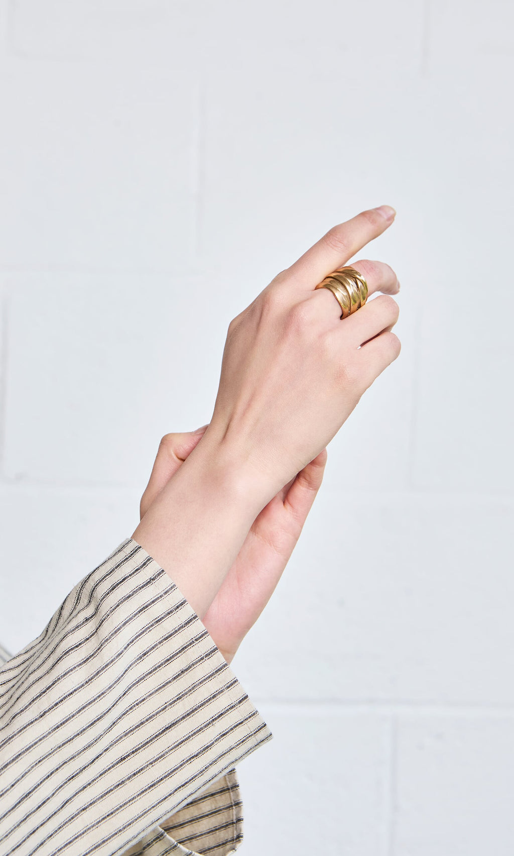Plümo- A hand wearing the Bobina Ring is raised, displaying this wearable art against a white brick background.