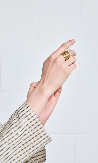 Plümo- A hand wearing the Bobina Ring is raised, displaying this wearable art against a white brick background.