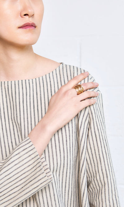 Plümo- A person in a striped shirt showcases the Bobina Ring and other gold rings as wearable art on their fingers.