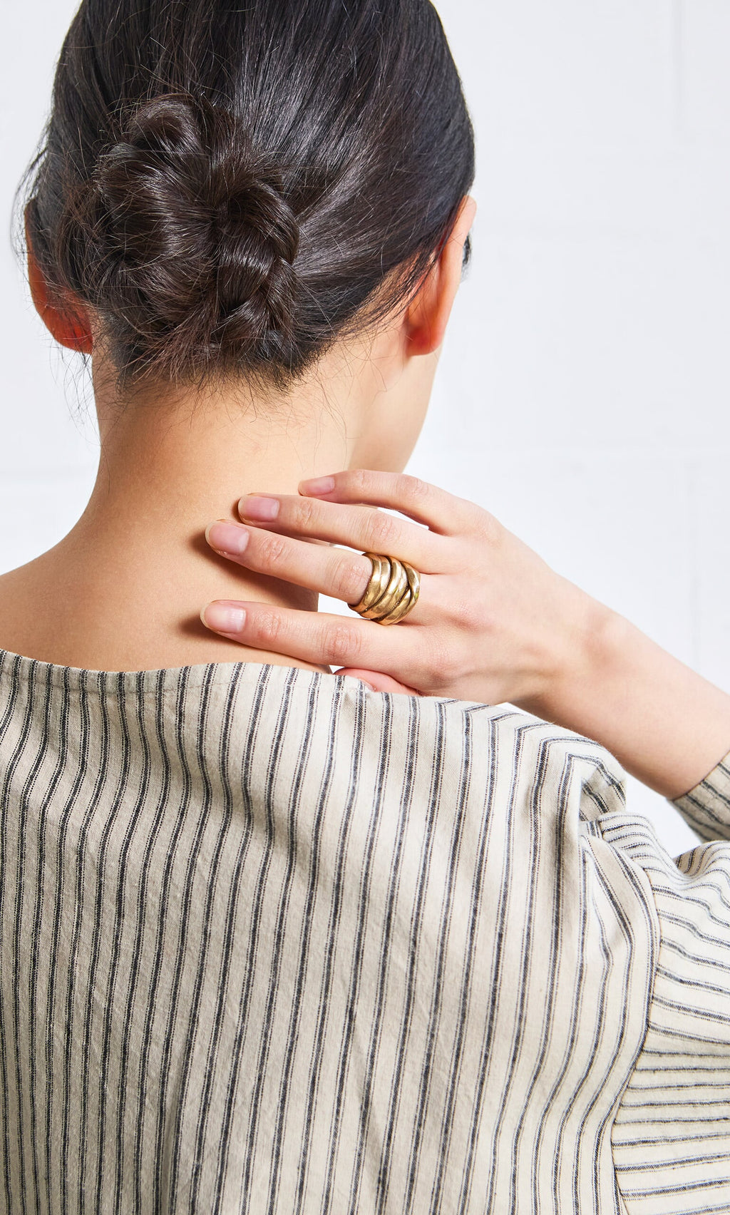 Plümo- Woman with a braided bun touches her neck, wearing the handmade Bobina Ring and a striped shirt, seen from behind.