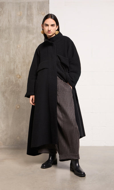 Plümo  Person in the Brabant Coat, pinstriped pants, and black boots stands on a polished concrete floor indoors.