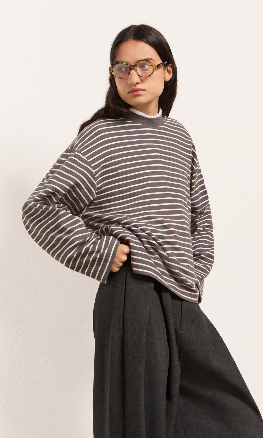 Plümo  Person in glasses wears the Breton Tee - Coal and wide-leg dark pants, standing against a light background.