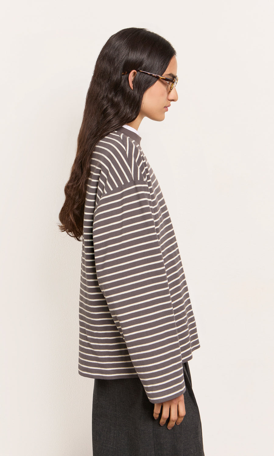 Plümo  Person with long dark hair and glasses models the Breton Tee - Coal in profile against a light background.