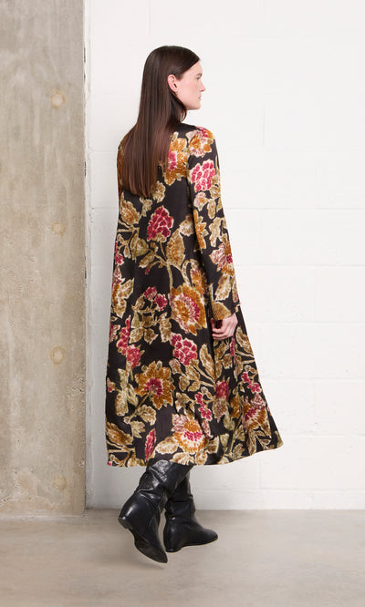 Plümo  Woman in the Brunn Dress and black boots stands sideways near a concrete and white brick wall.