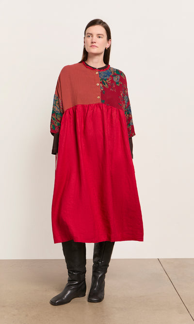 Plümo  Woman in the Burns Patchwork Dress, midi-length with florals, styled with black boots against a plain backdrop.