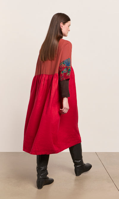 Plümo  Woman in the Burns Patchwork Dress with floral sleeves and black boots, walking on a beige floor.
