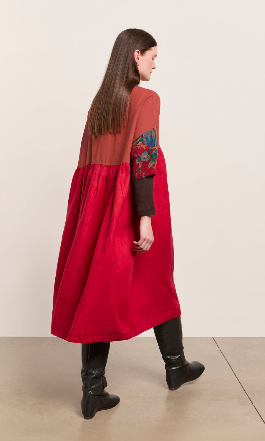 Plümo  Woman in the Burns Patchwork Dress with floral sleeves and black boots, walking on a beige floor.