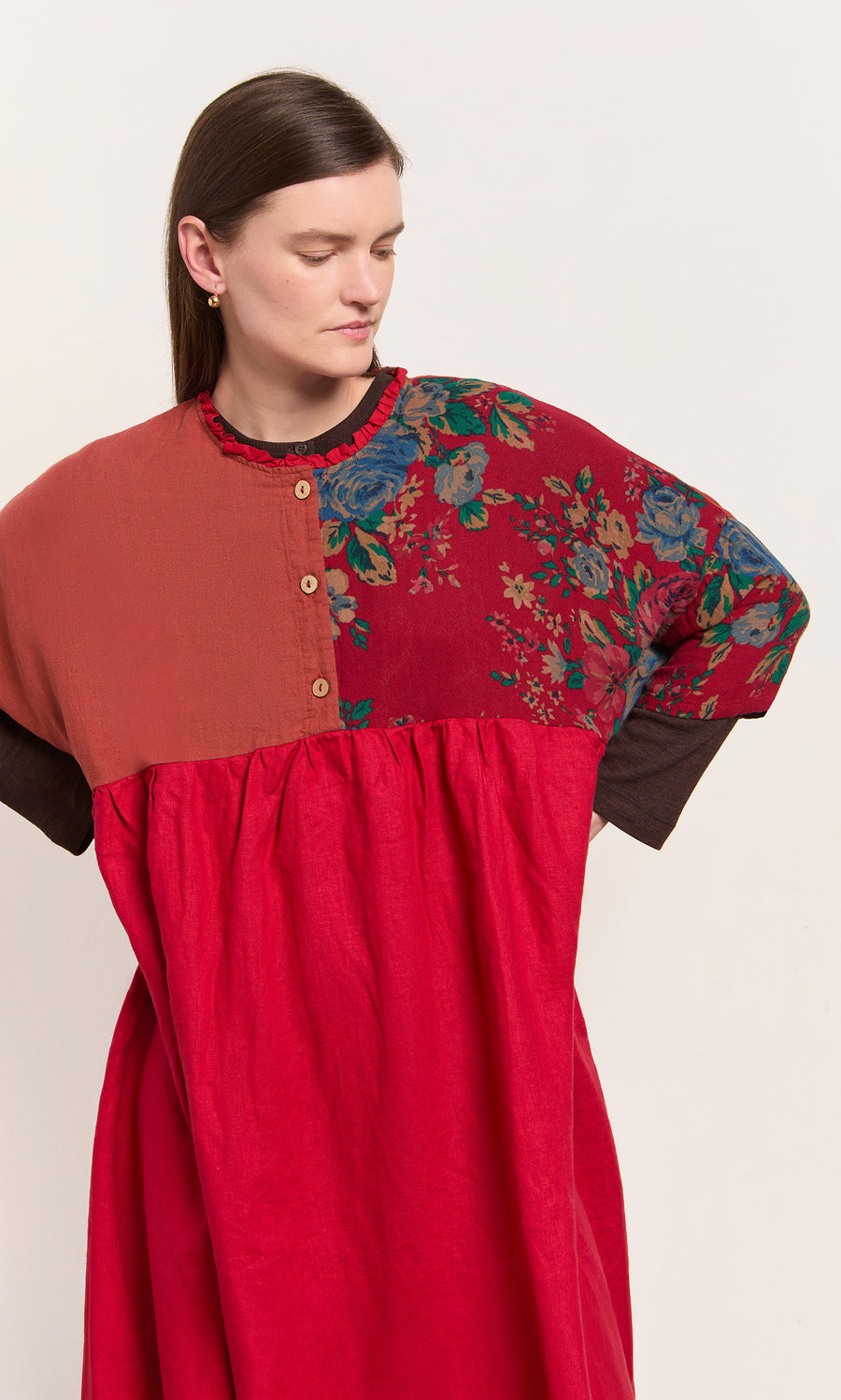 Plümo  Woman in the Burns Patchwork Dress—red linen with floral and solid panels, hands on hips, looking down.
