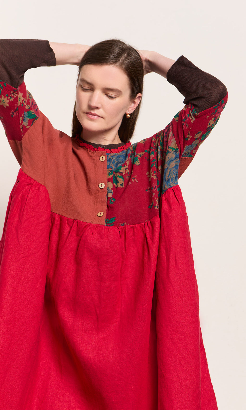Plümo  A woman in the Burns Patchwork Dress lifts her arms, eyes closed, against a plain background.