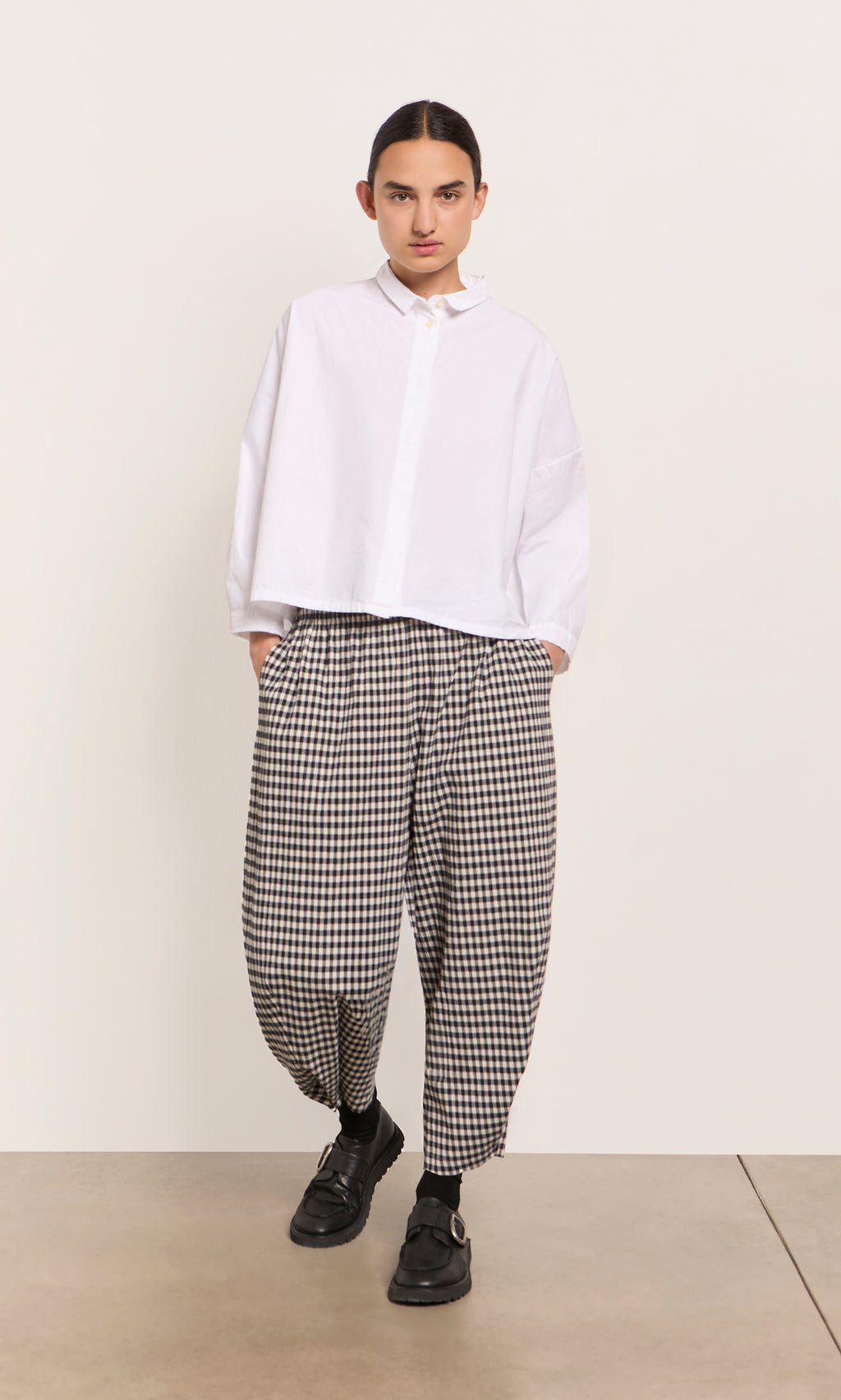 Plümo  Person in a loose white shirt and Butoni Pants - Black and White, hands in pockets against a plain background.
