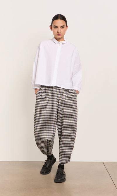 Plümo  Person in a loose white shirt and Butoni Pants - Black and White, hands in pockets against a plain background.