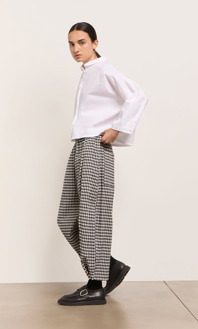 Plümo  Person in a white shirt and Butoni Pants - Black and White stands sideways in black shoes on a light background.