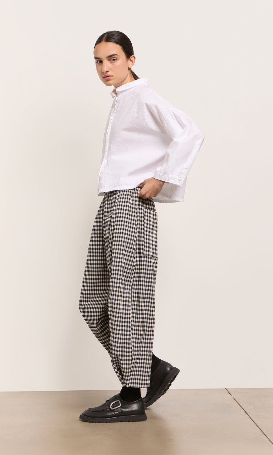 Plümo  Person in a white shirt and Butoni Pants - Black and White stands sideways in black shoes on a light background.